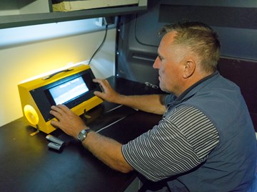 Mann an einem Tisch blickt auf das Display einer gelben Anlage, an der er mit beiden Händen arbeitet Mann an einem Tisch blickt auf das Display einer gelben Anlage, an der er mit beiden Händen arbeitet