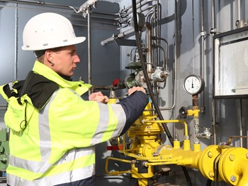 Junger Mitarbeiter in Warnschutzjacke und Helm arbeitet mit Schraubenschlüssel an einer Anlage Junger Mitarbeiter in Warnschutzjacke und Helm arbeitet mit Schraubenschlüssel an einer Anlage