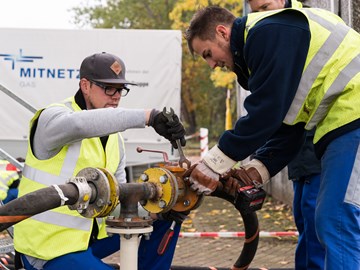 Zwei Mitarbeiter arbeiten mit Werkzeugen an einer Leitung auf einer Straße Zwei Mitarbeiter arbeiten mit Werkzeugen an einer Leitung auf einer Straße