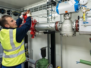 Mitarbeiter schraubt am Ventil einer Anlage Mitarbeiter schraubt am Ventil einer Anlage