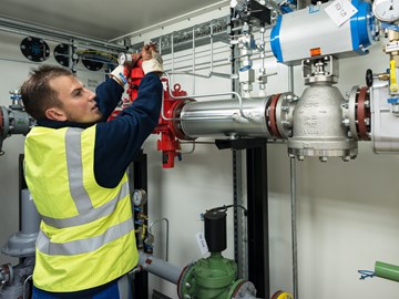 Mitarbeiter schraubt am Ventil einer Anlage Mitarbeiter schraubt am Ventil einer Anlage