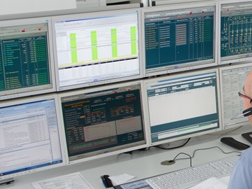 Mitarbeiter mit Headset sitzt an einem Tisch vor einer Tastatur und blickt auf acht Monitore Mitarbeiter mit Headset sitzt an einem Tisch vor einer Tastatur und blickt auf acht Monitore