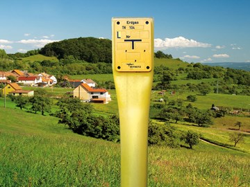 Erdgas-Schieber vor einer grünen, hügeligen Landschaft mit einer kleinen Stadt Erdgas-Schieber vor einer grünen, hügeligen Landschaft mit einer kleinen Stadt