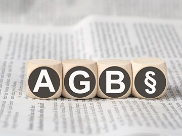 Vier Holzwürfel auf einer Zeitung zeigen die Abkürzung AGB und das Paragrafenzeichen Vier Holzwürfel auf einer Zeitung zeigen die Abkürzung AGB und das Paragrafenzeichen