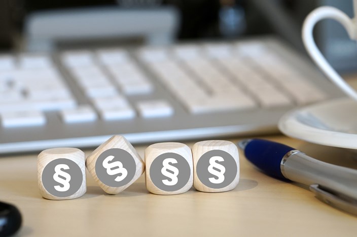 Vier Holzwürfel auf einem Schreibtisch neben einem Kugelschreiber vor einer Tastatur zeigen alle das Paragrafenzeichen Vier Holzwürfel auf einem Schreibtisch neben einem Kugelschreiber vor einer Tastatur zeigen alle das Paragrafenzeichen